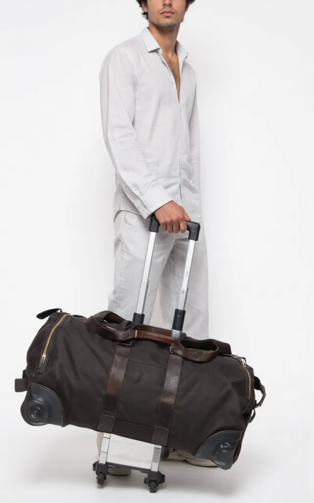 A French male model with a Duffle bag with wheels, wearing a shirt, against a white background, in a front   facing close   up